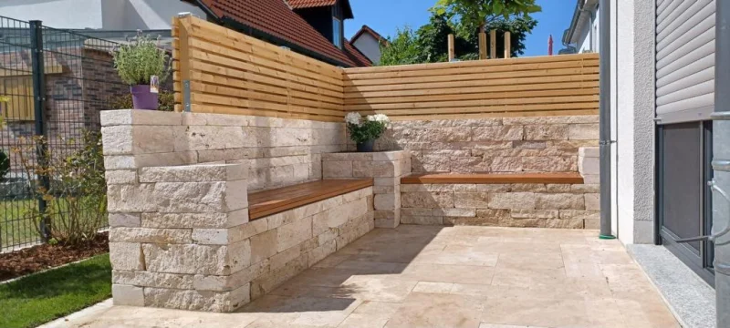 Eckbereich einer Travertin Gartenmauer mit zwei Holzsitzbänken