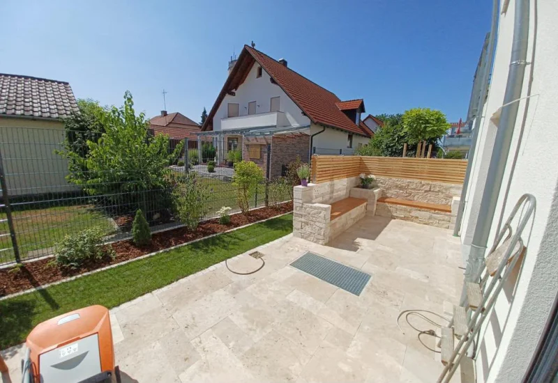 Gartenansicht mit Travertin Sitzmauer, Rasenfläche und Nachbarhaus im Hintergrund